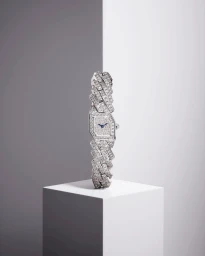 Diamond-encrusted luxury watch displayed vertically on a white pedestal in a minimalist studio setting.