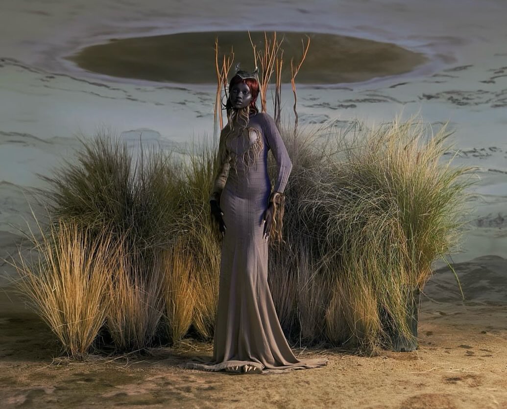 Dark-skinned woman in a long gown, standing in a surreal landscape with sparse vegetation, against a lake-like background under soft lighting.