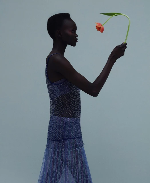 Profile view of a dark-skinned woman in a sparkling dress holding a tulip in a studio setting, focusing on fashion and artistic expression.