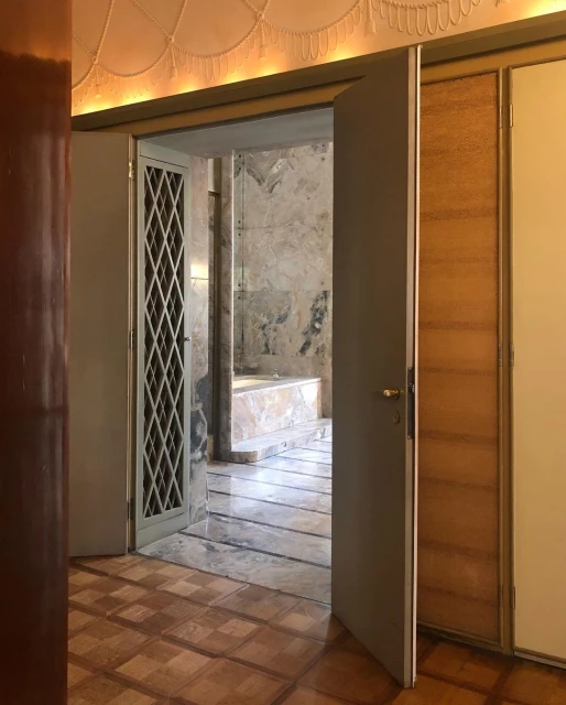 Open doorway reveals a glimpse into a marble bathroom with a bathtub, complemented by an ornate ceiling in a home interior setting.