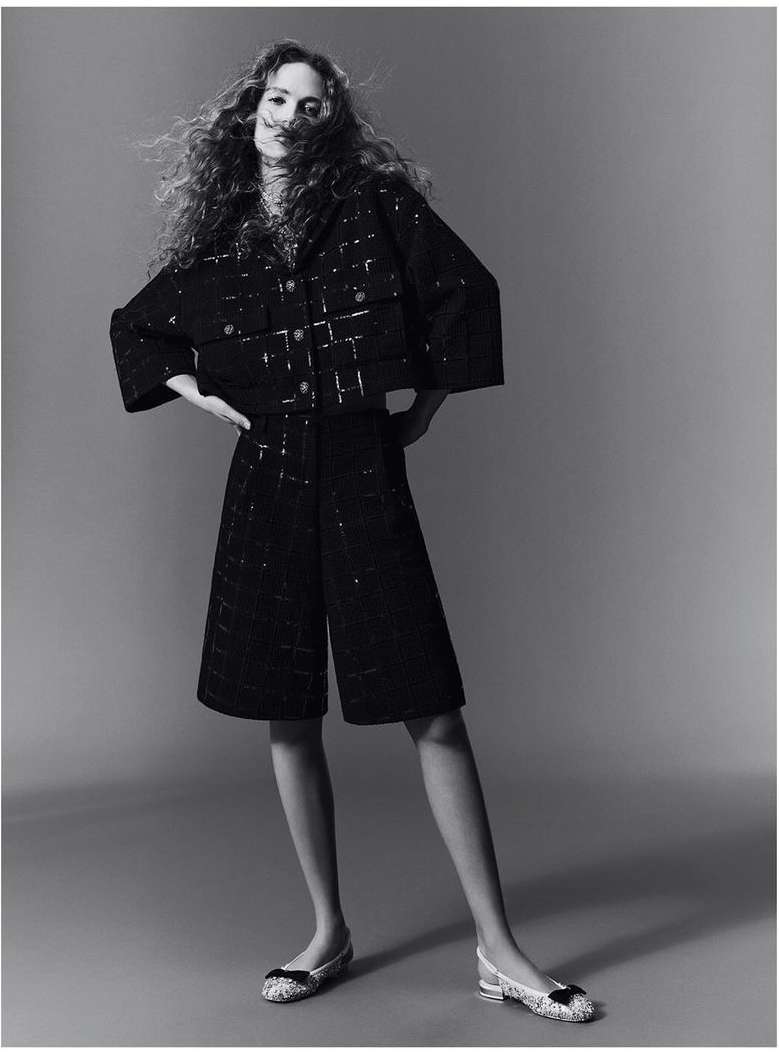 Model with long curly hair wearing a dark textured matching jacket and shorts against a neutral studio backdrop