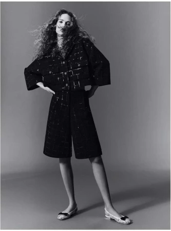 Model with long curly hair wearing a dark textured matching jacket and shorts against a neutral studio backdrop