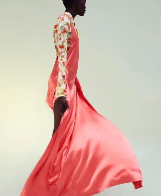Runway fashion: An adult woman models a vibrant coral slip dress paired with a floral print blouse against a soft, neutral backdrop.