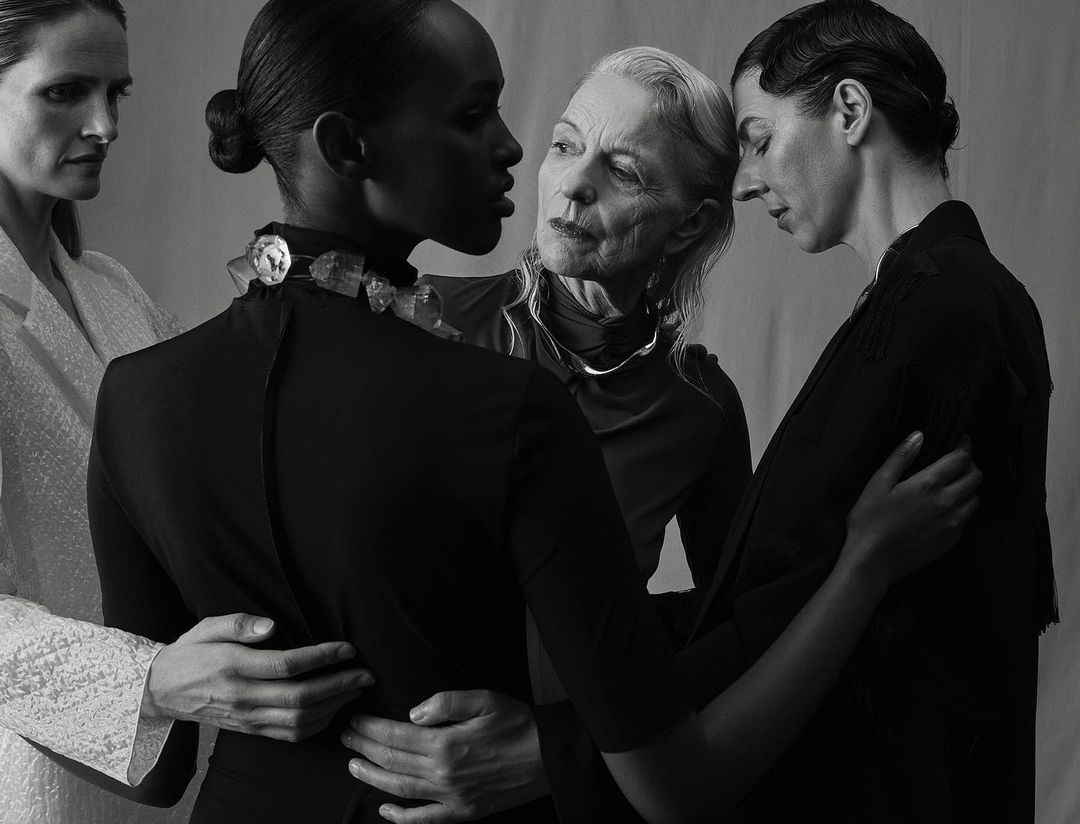 Monochrome portrait of four adult women of varying ages in dark, modern clothing posing in a studio with neutral background.