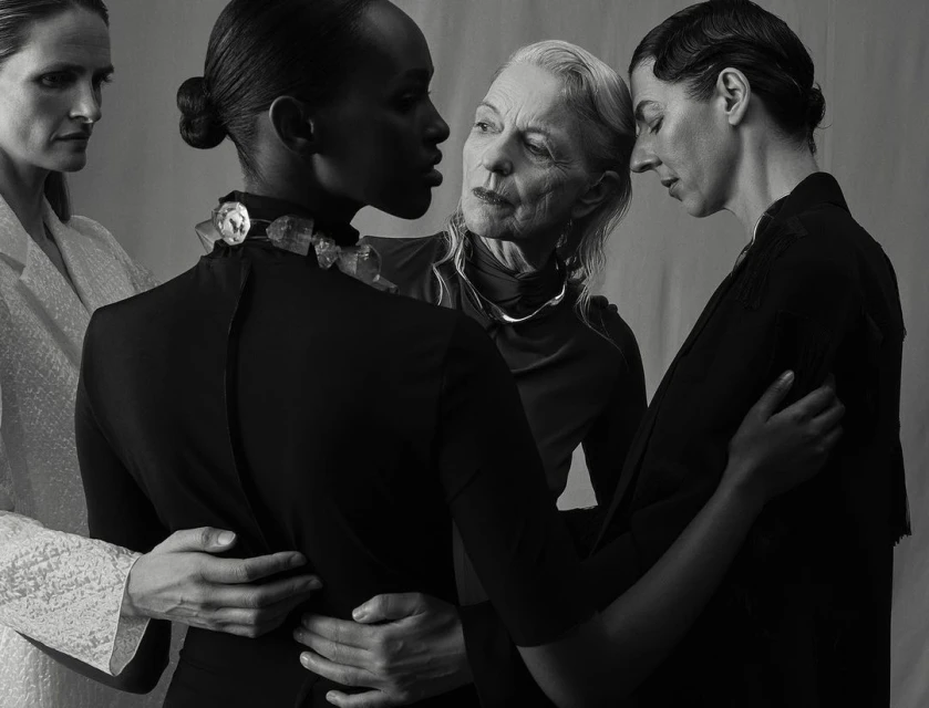 Monochrome portrait of four adult women of varying ages in dark, modern clothing posing in a studio with neutral background.