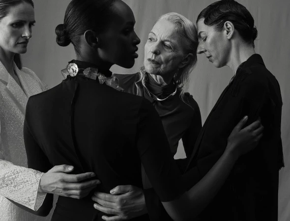 Monochrome portrait of four adult women of varying ages in dark, modern clothing posing in a studio with neutral background.