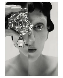 Close-up monochrome portrait of a model holding a large metallic rose earring with a pearl charm near her face.