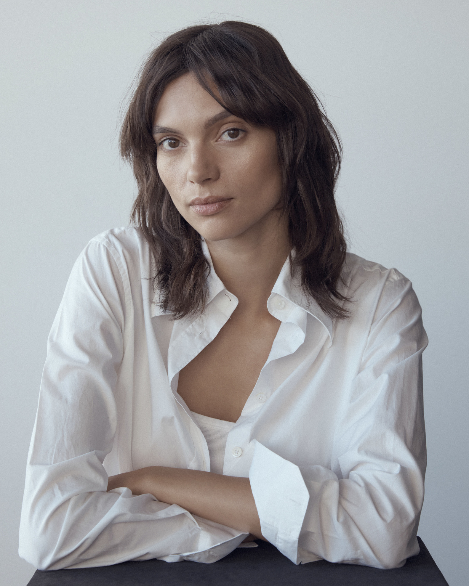 Portrait of an adult woman with medium brown hair, wearing a white collared shirt, posing indoors against a neutral background.
