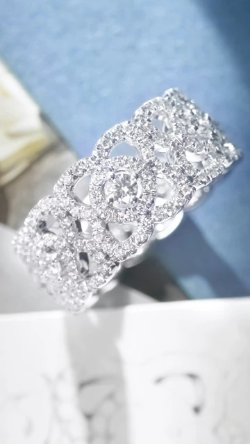 Close-up of an intricately designed diamond ring with floral patterns, set against a soft blue background, highlighting the jewelry's brilliance.