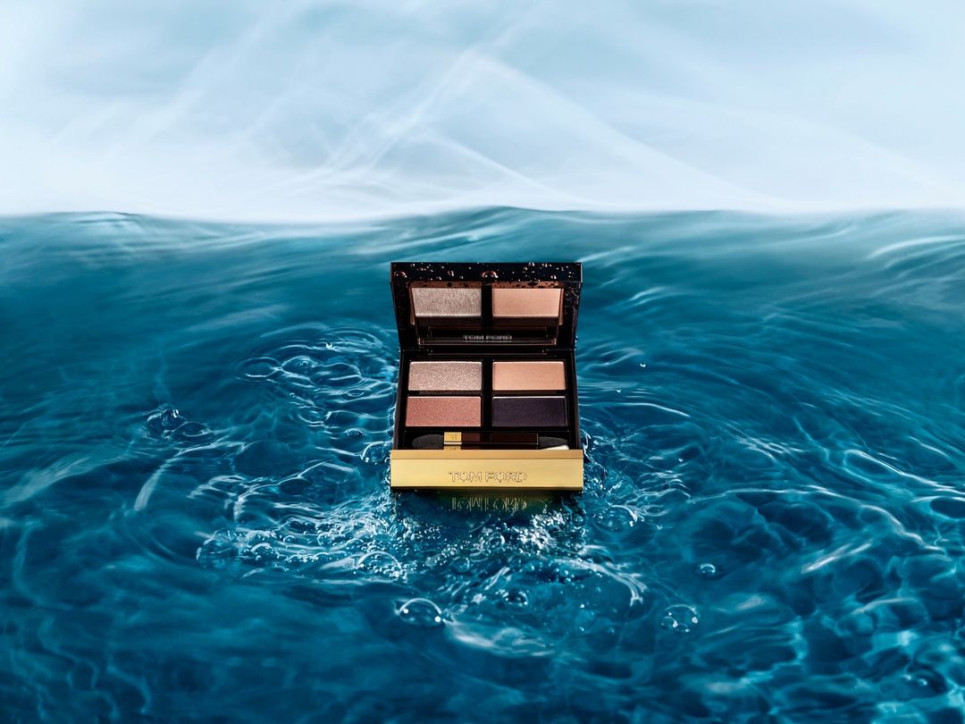 Tom Ford eyeshadow palette displayed above a surface of blue water ripples against a light blue sky backdrop. Beauty product photography.