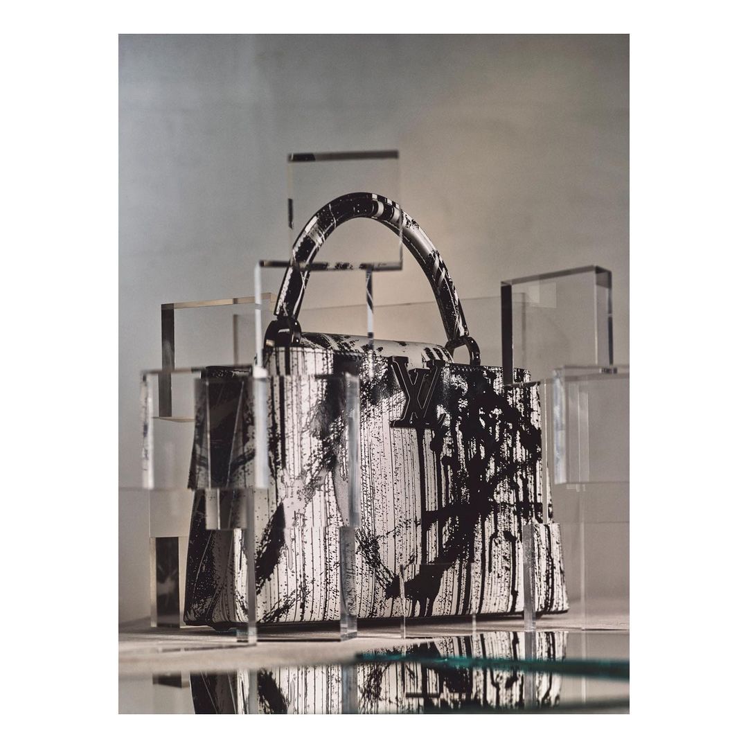 Luxury Louis Vuitton purse with black and white graphic paint, displayed among geometric acrylic cubes in a minimalist fashion shoot.