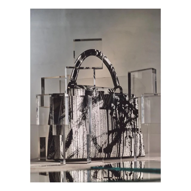 Luxury Louis Vuitton purse with black and white graphic paint, displayed among geometric acrylic cubes in a minimalist fashion shoot.