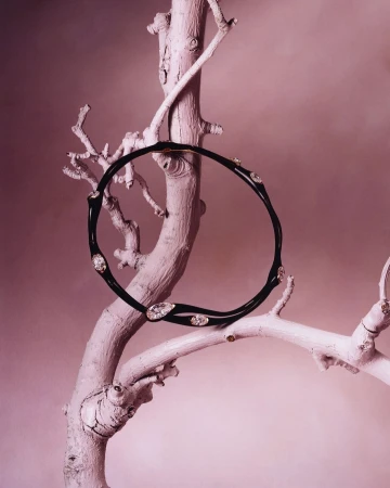 Black and diamond necklace on a textured white branch against a pink backdrop in a studio product shot for a jewelry campaign.
