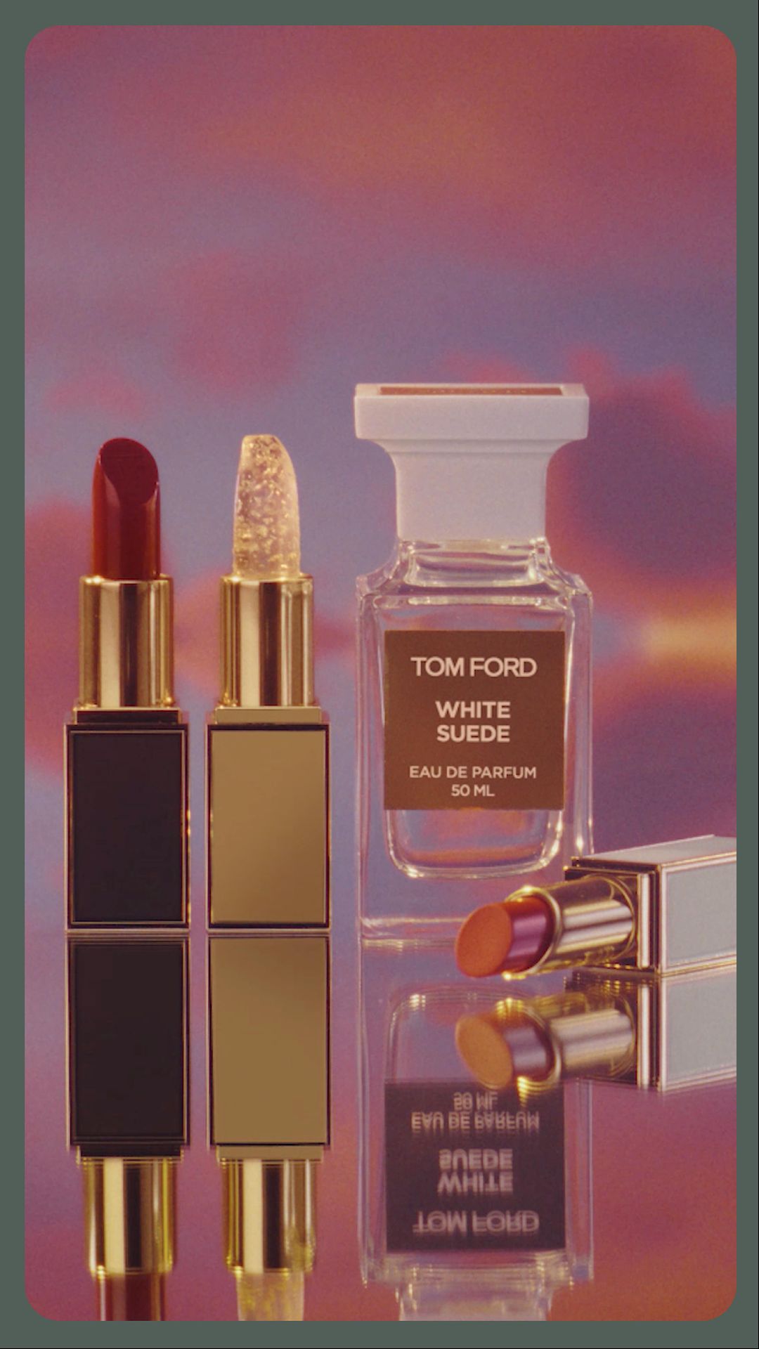 Cosmetic still life: Tom Ford lipsticks and White Suede eau de parfum on a reflective surface, with a pink and orange clouded background.