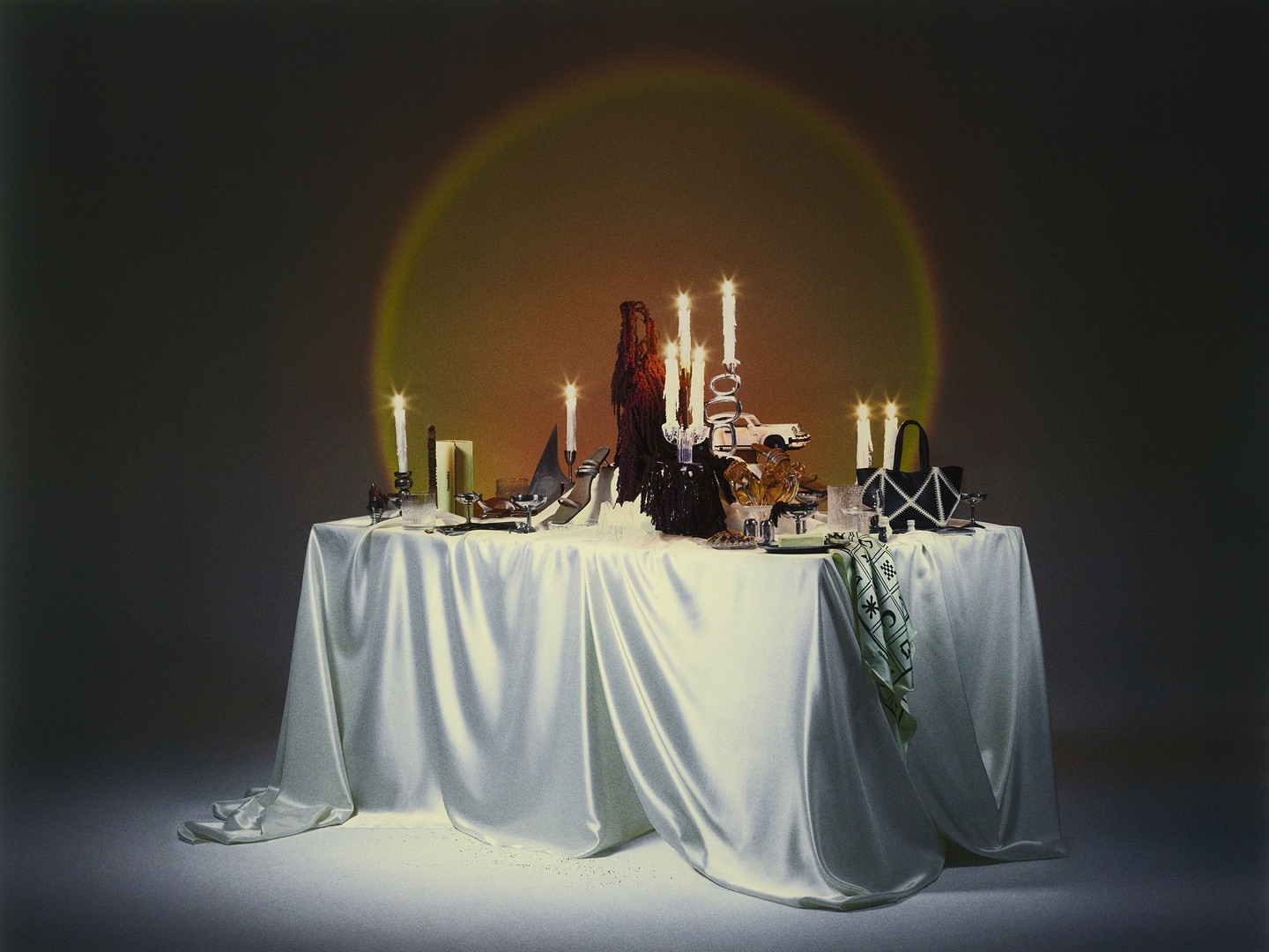 Table arrangement with candles, shoes, handbags, and other decorative items under a spotlight, creating an elegant and sophisticated still life.