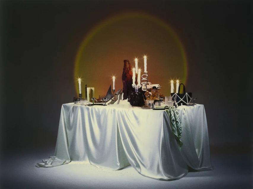 Table arrangement with candles, shoes, handbags, and other decorative items under a spotlight, creating an elegant and sophisticated still life.