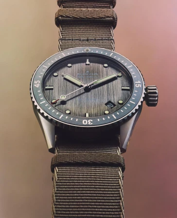 Close-up of a Blancpain watch with a textured gray dial, silver case, and an olive green nylon strap displayed on a neutral backdrop.
