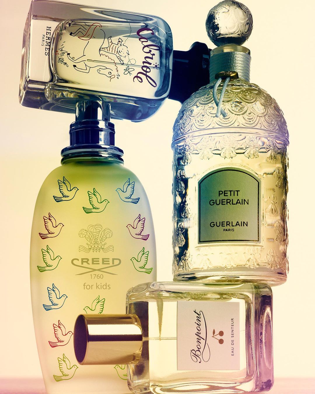 Four perfume bottles of different shapes and sizes are stacked against a neutral background, featuring designer brands such as Hermes and Creed.