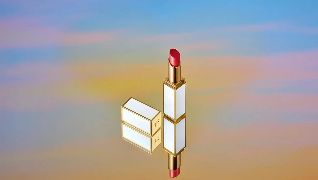 Close-up of red lipstick in gold and white packaging, one standing upright and another lying down, against a colourful background.