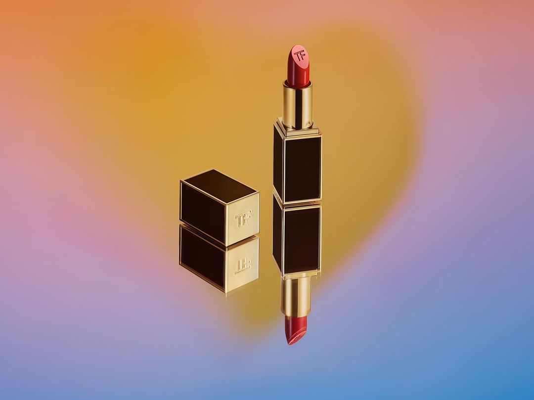 Still life studio shot of red lipstick with gold and black casing on a colorful yellow and purple gradient backdrop. Beauty product.