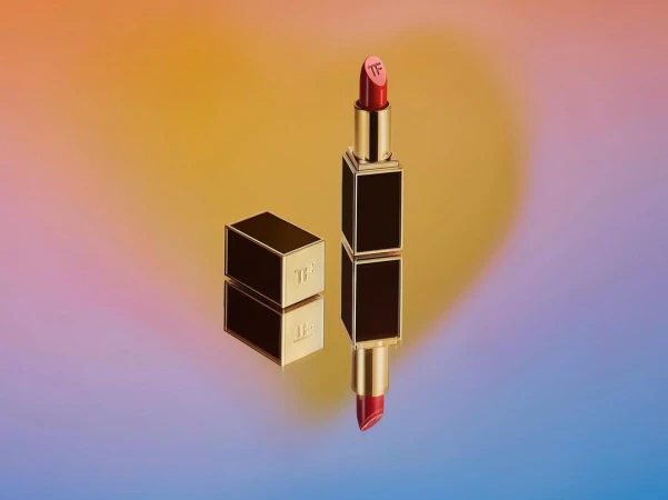 Still life studio shot of red lipstick with gold and black casing on a colorful yellow and purple gradient backdrop. Beauty product.
