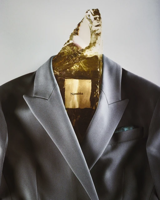 Still life shot of a grey blazer with a decorative crystal, metallic gold embellishment, and a designer label for search optimization.