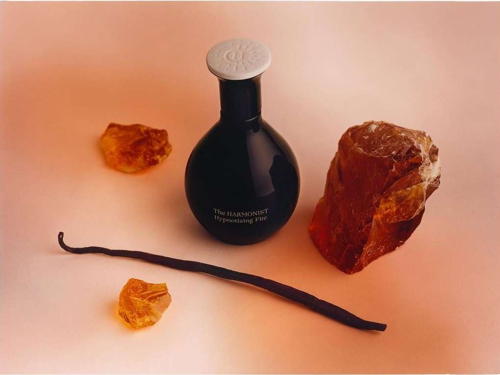 Still life shot of a perfume bottle, vanilla bean and amber stones on a peach background, showcasing beauty product and natural elements.
