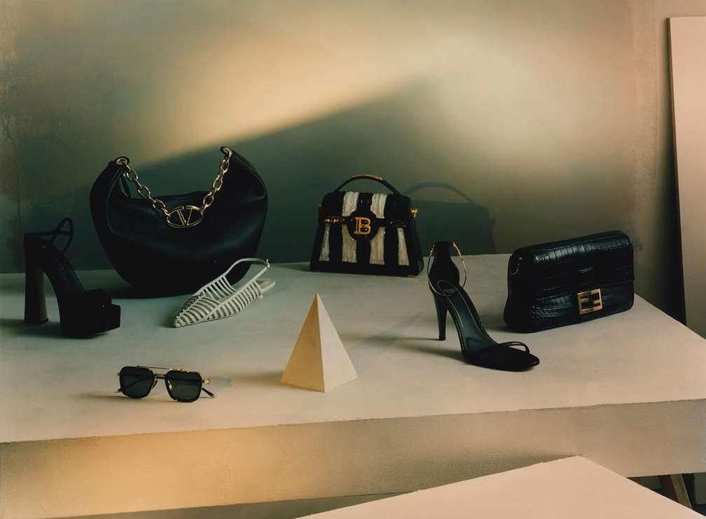 Fashion still life: Black leather handbags and high heel shoes from designer brands arranged on a stepped platform with a pyramid prop.