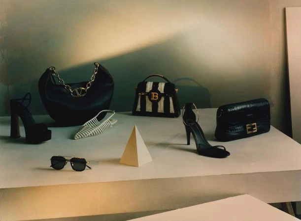 Fashion still life: Black leather handbags and high heel shoes from designer brands arranged on a stepped platform with a pyramid prop.