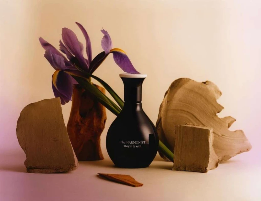 Still life featuring a black perfume bottle with white accents, complemented by purple iris flowers and abstract wooden blocks.