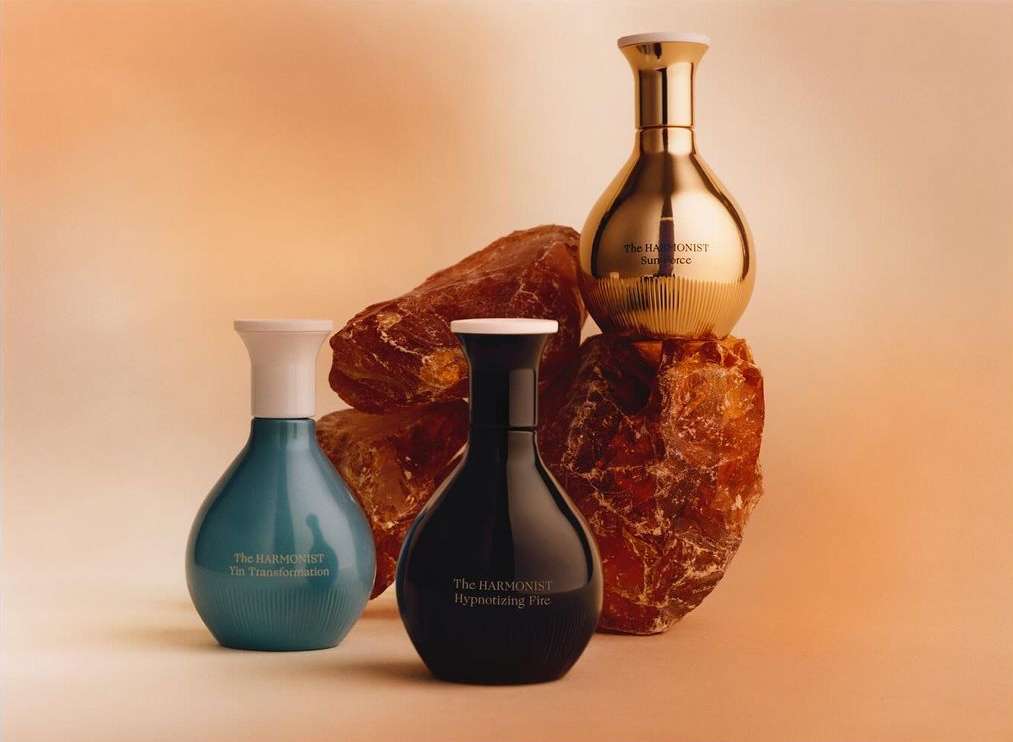 Still life featuring four decorative glass perfume bottles in blue, black and gold, displayed on textured brown stone fragments.