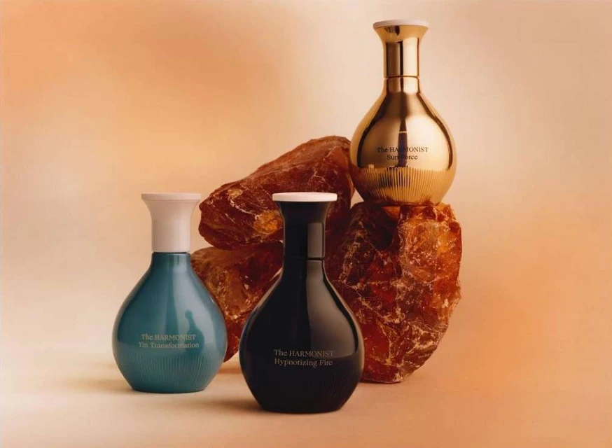 Still life featuring four decorative glass perfume bottles in blue, black and gold, displayed on textured brown stone fragments.