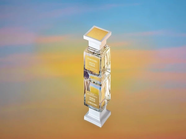 Tom Ford White Suede fragrance bottle on a mirrored surface with a diffused yellow and blue background, product shot, beauty.