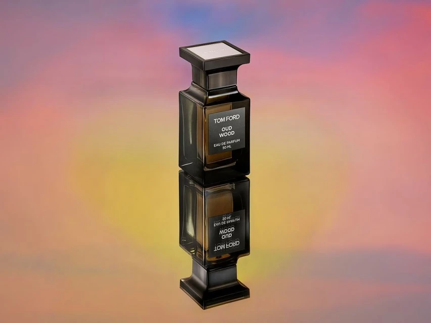 Tom Ford Oud Wood perfume bottle reflecting on surface with a colorful background. Luxurious and elegant fragrance presentation.