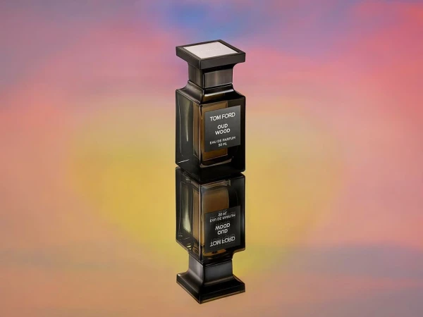 Tom Ford Oud Wood perfume bottle reflecting on surface with a colorful background. Luxurious and elegant fragrance presentation.