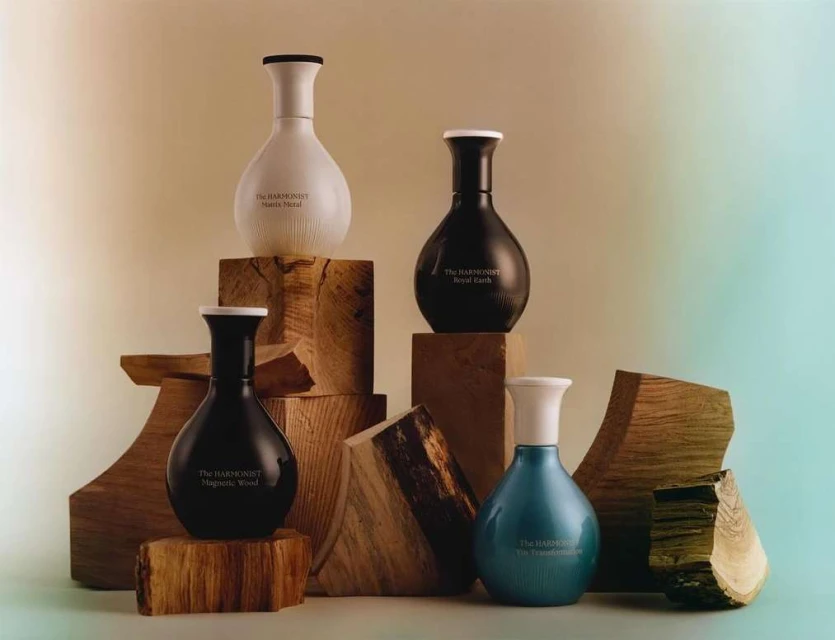 Four perfume bottles in different colors are displayed on wooden blocks against a soft, gradient background in a studio setting.