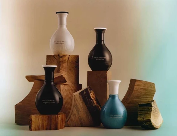 Four perfume bottles in different colors are displayed on wooden blocks against a soft, gradient background in a studio setting.