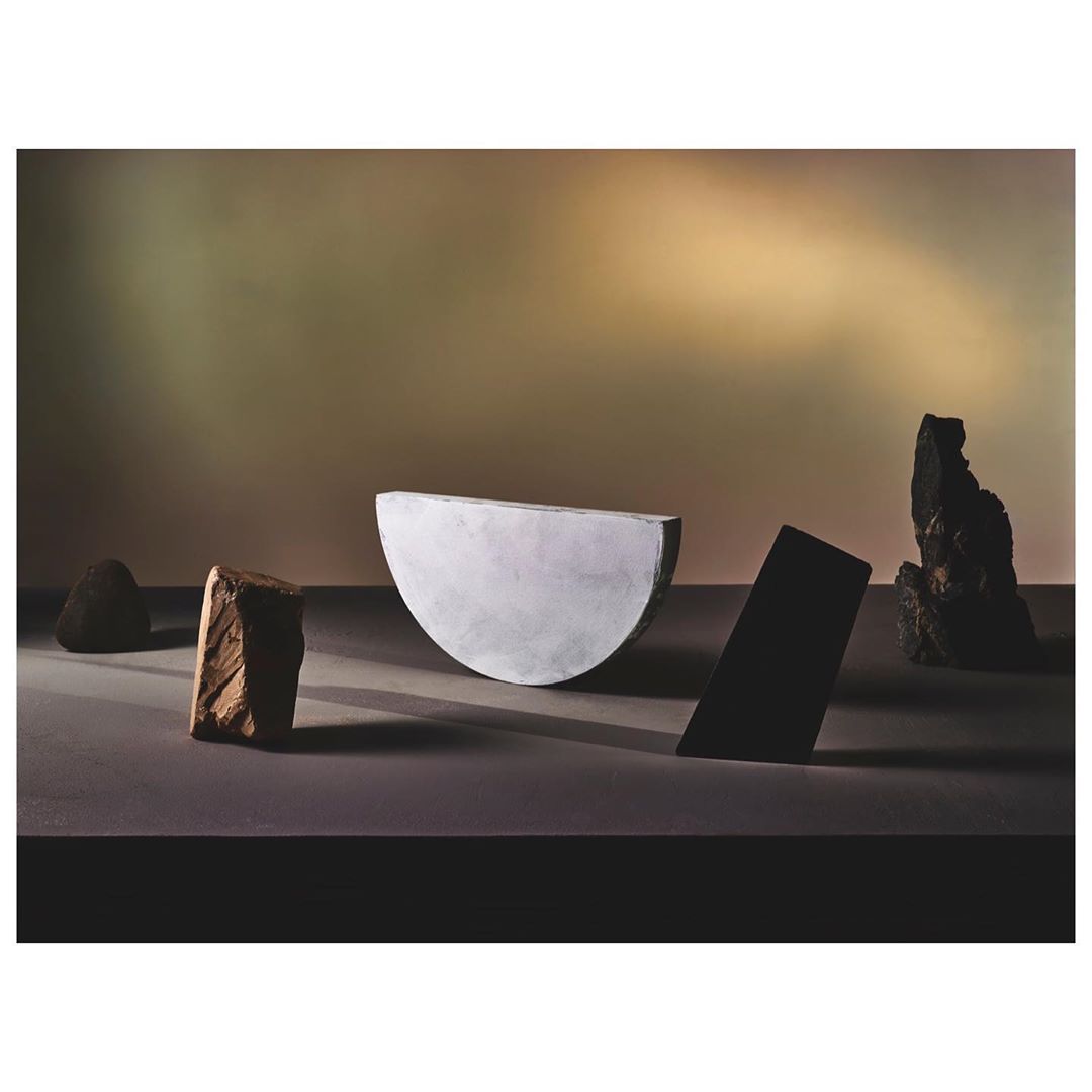 Studio still life with geometric shapes and rocks on a smooth surface, highlighted by soft, diffused light and muted earthy tones.