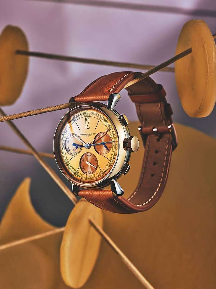 Close-up studio shot of an elegant wristwatch with a leather band, floating among abstract golden decorative shapes on a lavender background.