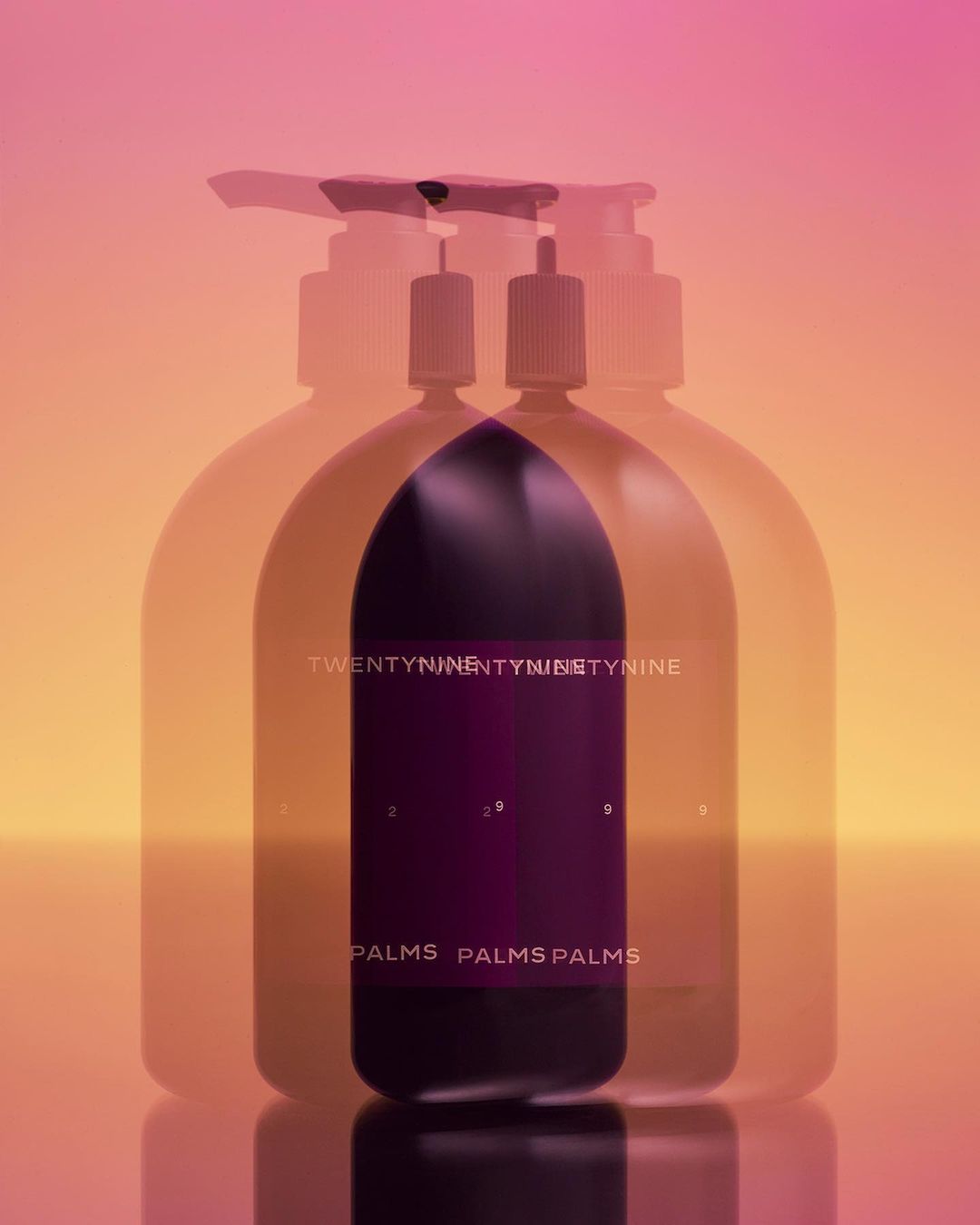 Minimalist product shot of a purple soap dispenser with a pump top, featuring layered transparency against a blended pink and orange backdrop.