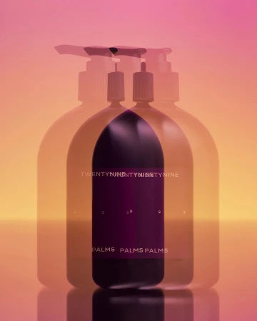 Minimalist product shot of a purple soap dispenser with a pump top, featuring layered transparency against a blended pink and orange backdrop.