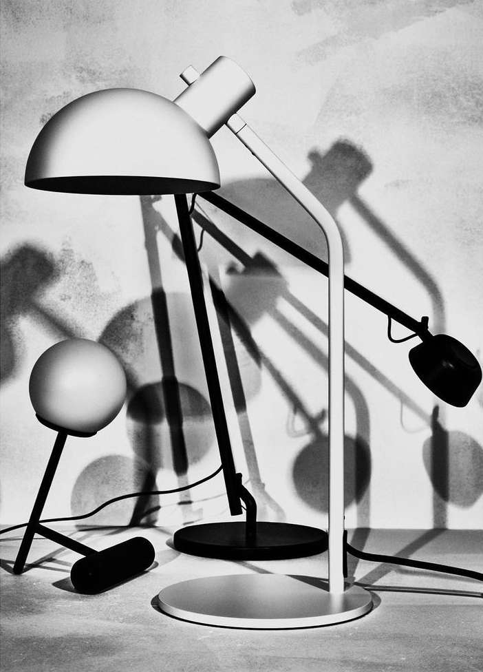 Monochrome product shot of two adjustable lamps with dome shades, positioned on a table against a textured wall casting stark shadows.