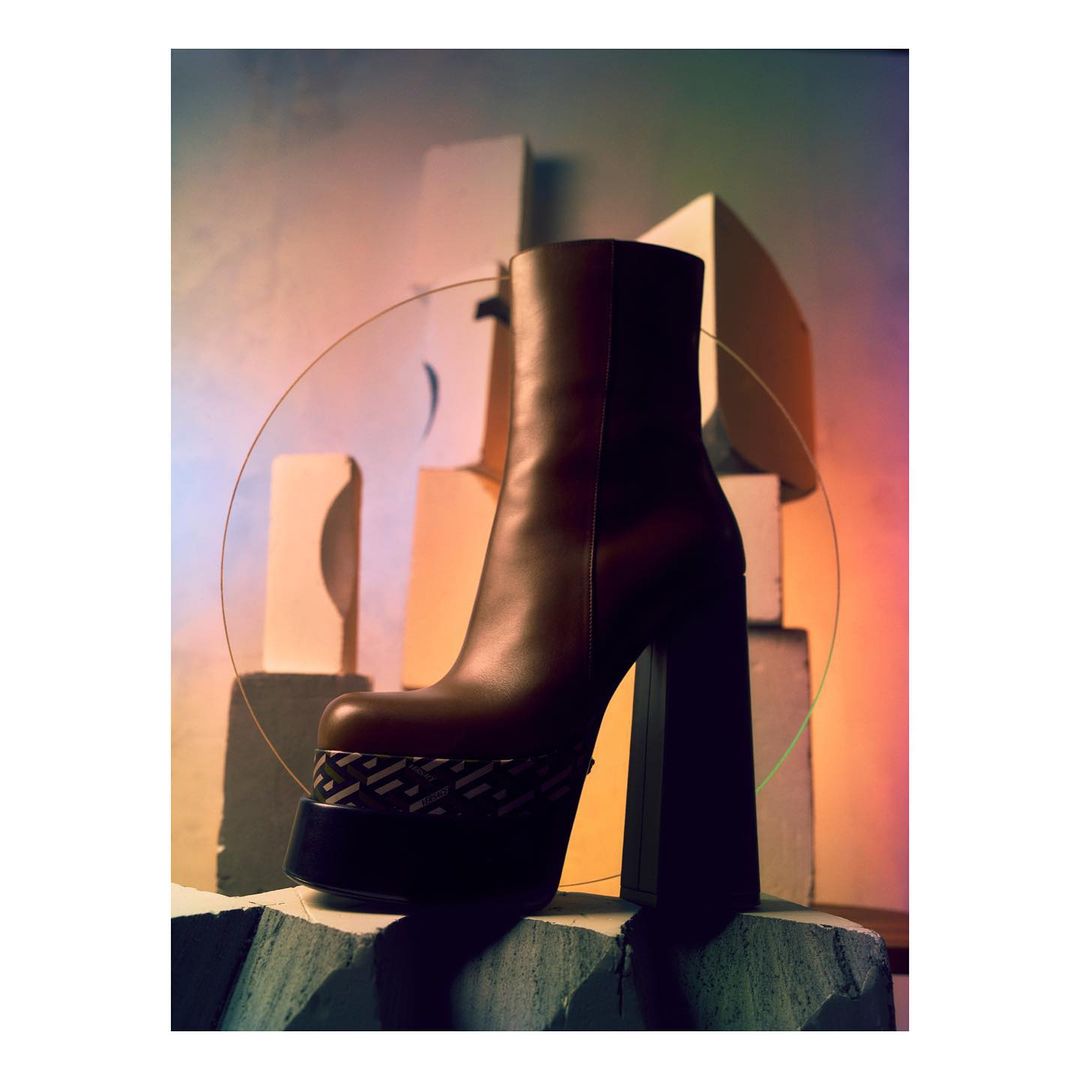 Brown leather platform boot with a geometric pattern, presented on a concrete-like block against a muted color block background with an iridescent circle.