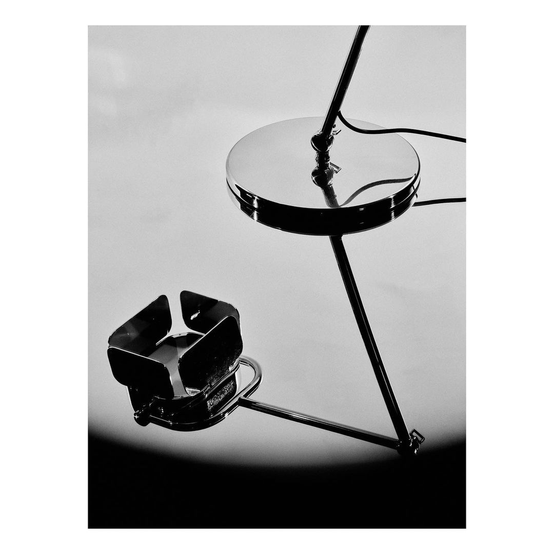 Monochrome product shot of a modern metal side table featuring a round tabletop and a geometric magazine rack, set against a gradient background.