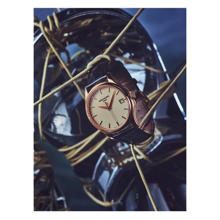 Wristwatch featuring a black leather strap and a cream-colored dial, displayed with tan cords and a metallic sphere in the background.