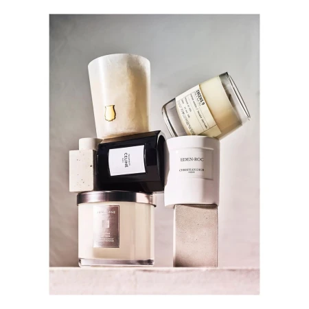 Assorted luxury candles from Celine, Christian Dior, and Jo Malone stacked on neutral concrete blocks in soft, diffused lighting.