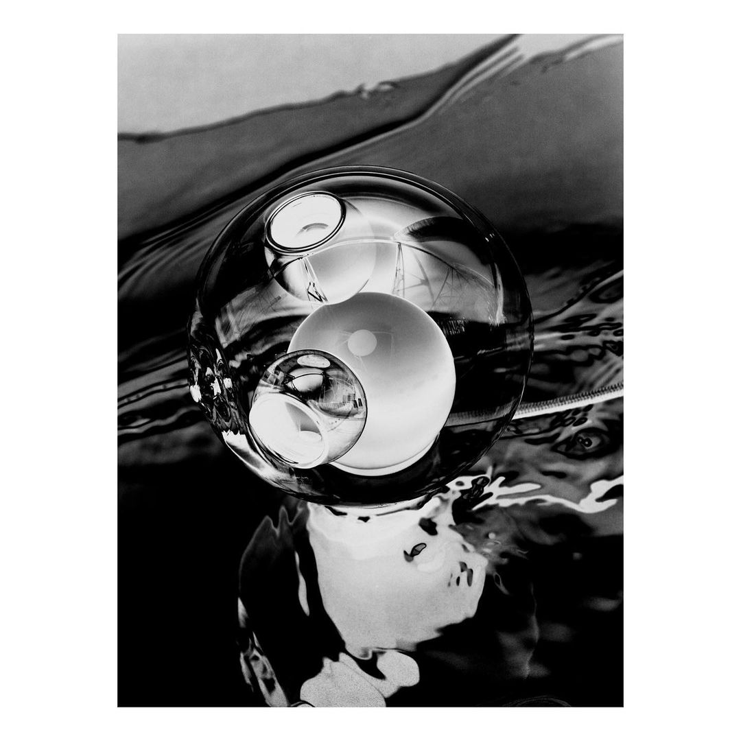 Black and white still life featuring transparent glass spheres refracting light, resting on a glossy surface with subtle water reflections.