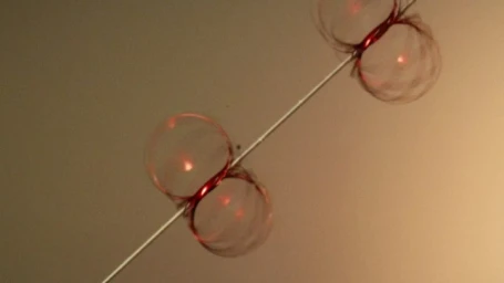 Transparent glass spheres pierced by a thin silver rod against a warm gradient background