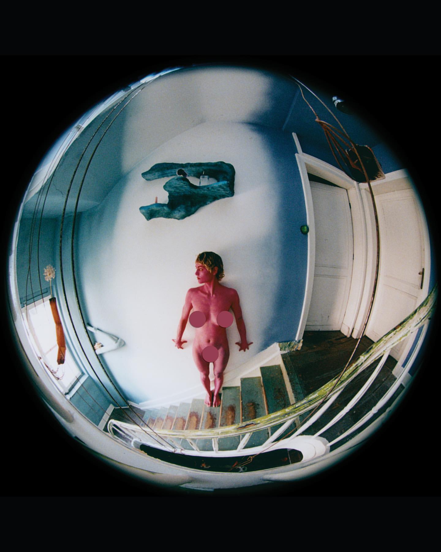 Top-down fisheye lens captures a fair-skinned adult female lying on white stairs in a blue and white room with decorative wall art.