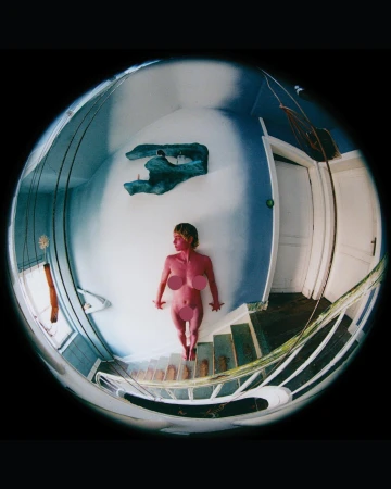 Top-down fisheye lens captures a fair-skinned adult female lying on white stairs in a blue and white room with decorative wall art.